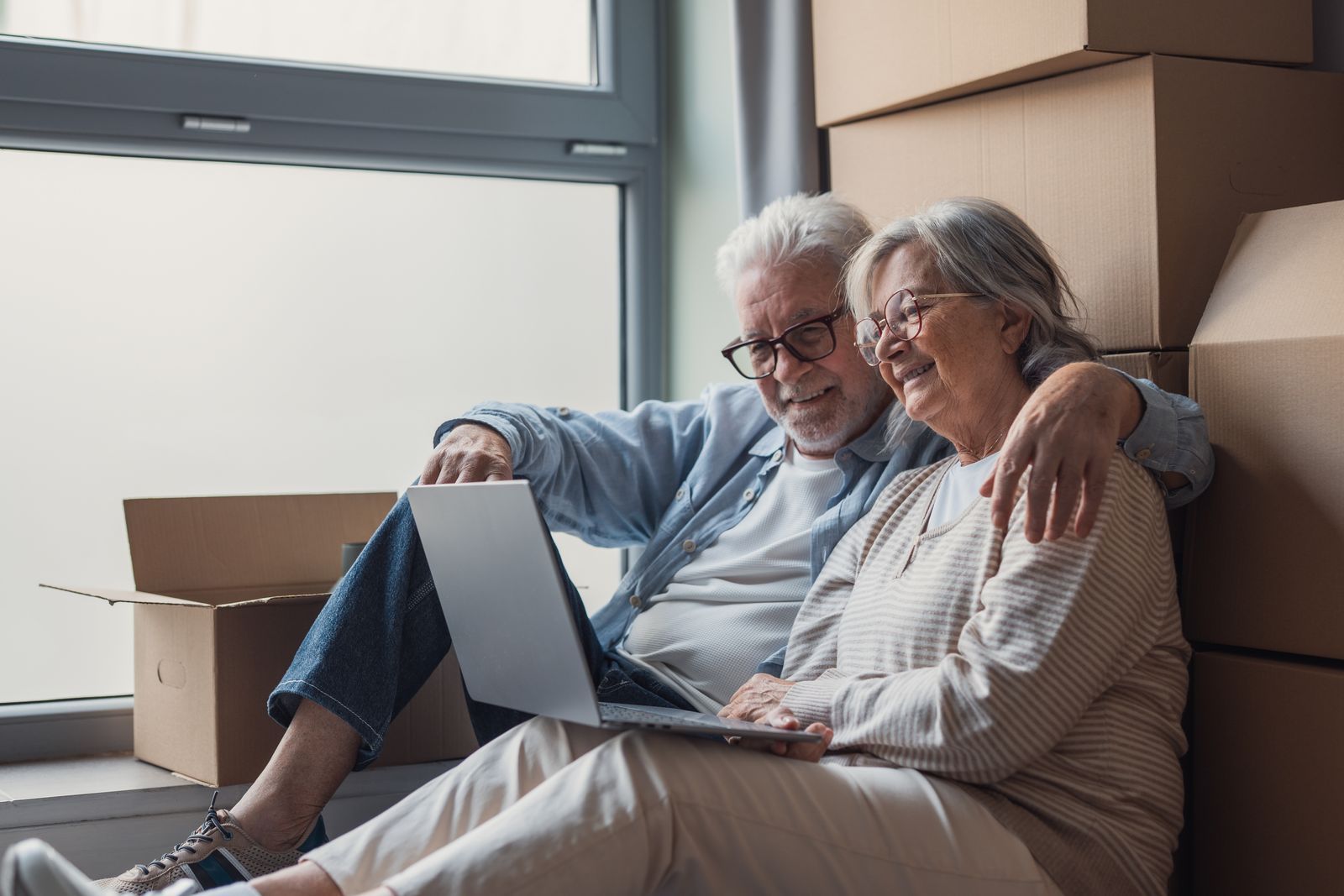 Seniorinnenpaar sitzt mit Laptop zwischen Umzugskartons in einer Hamburger Wohnung